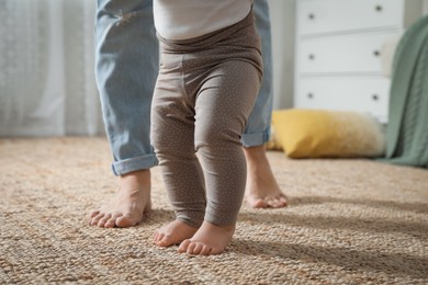 Photo of Mother supporting her baby daughter while she learning to walk at home, closeup