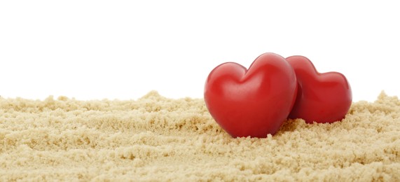 Photo of Honeymoon concept. Two red wooden hearts and sand isolated on white