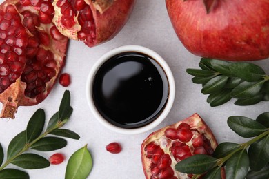 Photo of Tasty pomegranate sauce in bowl, branches and fruits on light table, flat lay