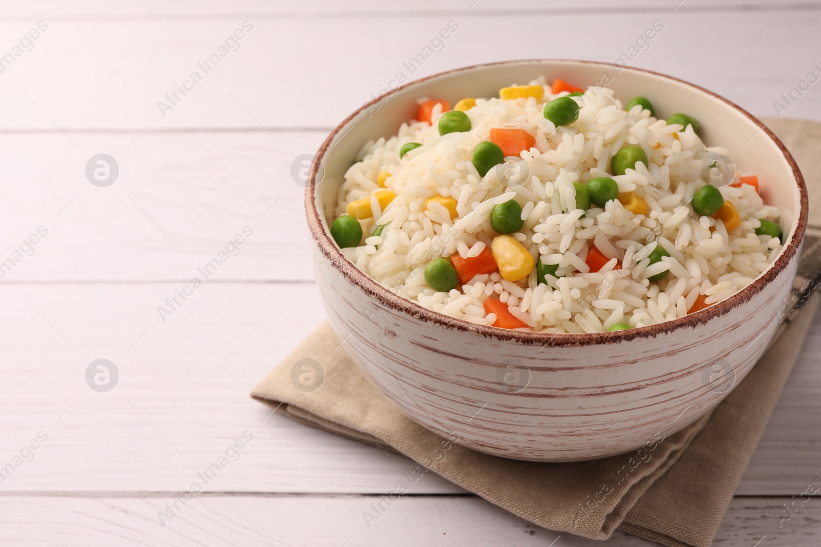 Photo of Bowl of delicious rice with vegetables on white wooden table, closeup. Space for text