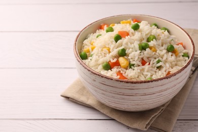 Bowl of delicious rice with vegetables on white wooden table, closeup. Space for text