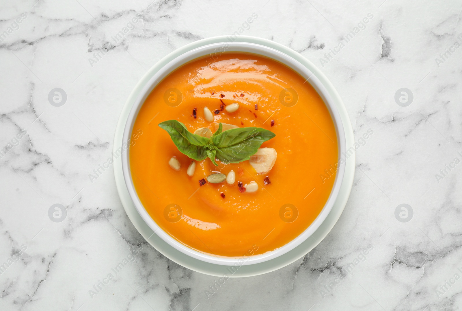 Photo of Delicious pumpkin soup in bowl on marble table, top view