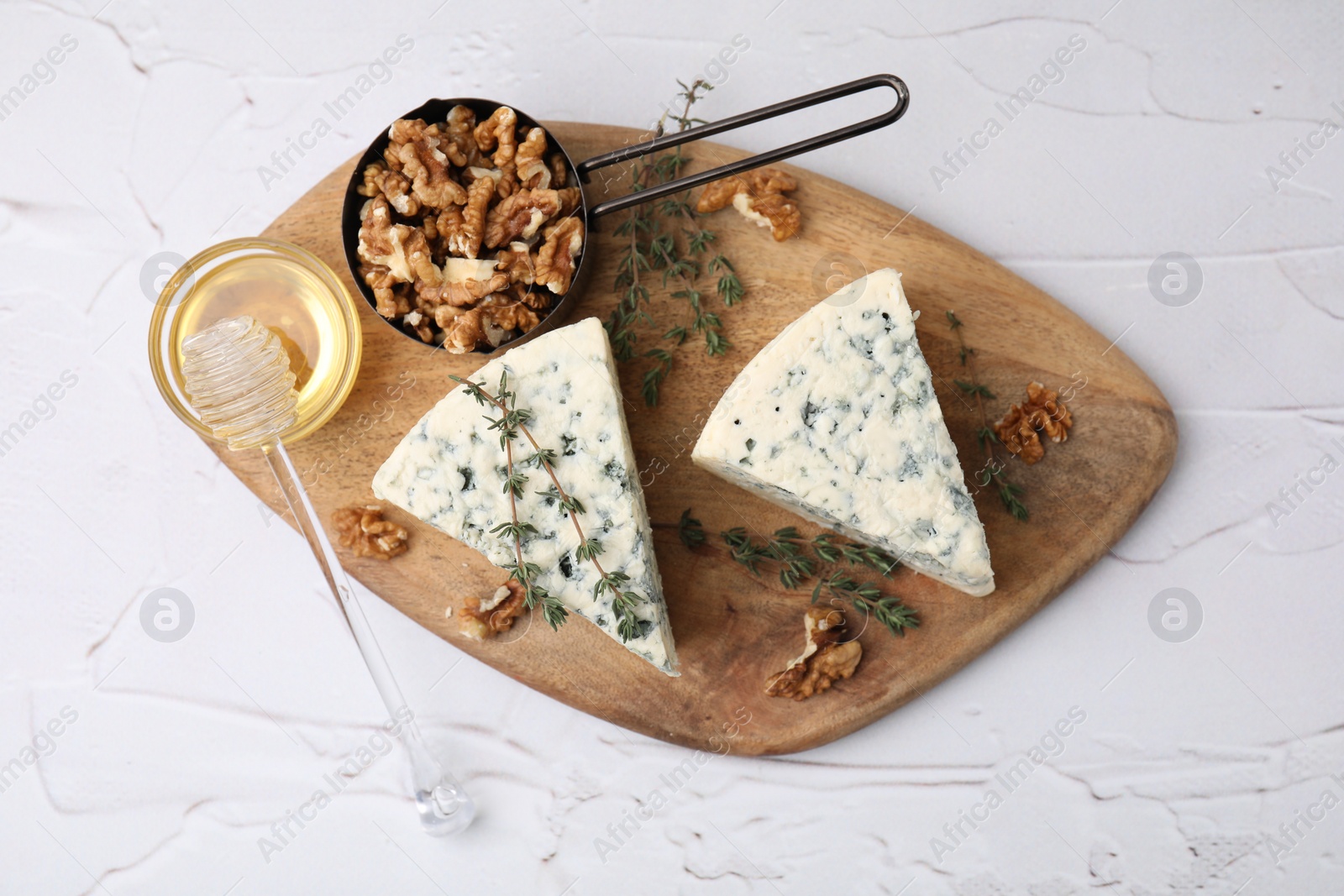 Photo of Tasty blue cheese with thyme, honey and walnuts on white textured table, top view