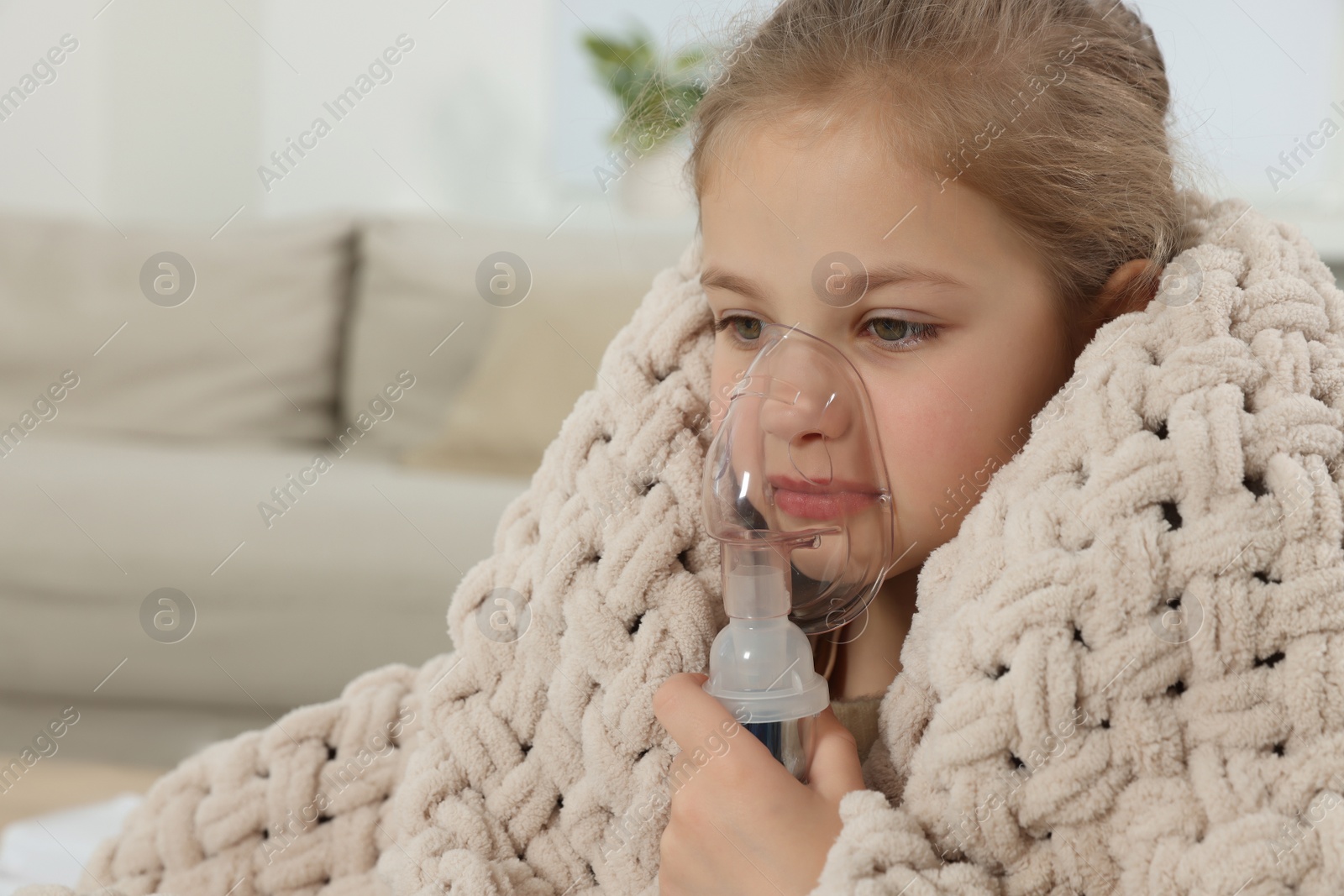 Photo of Little girl using nebulizer for inhalation at home