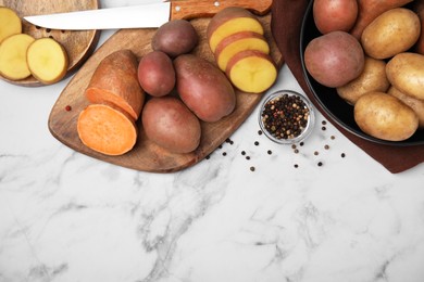 Different types of fresh potatoes on white marble table, flat lay. Space for text