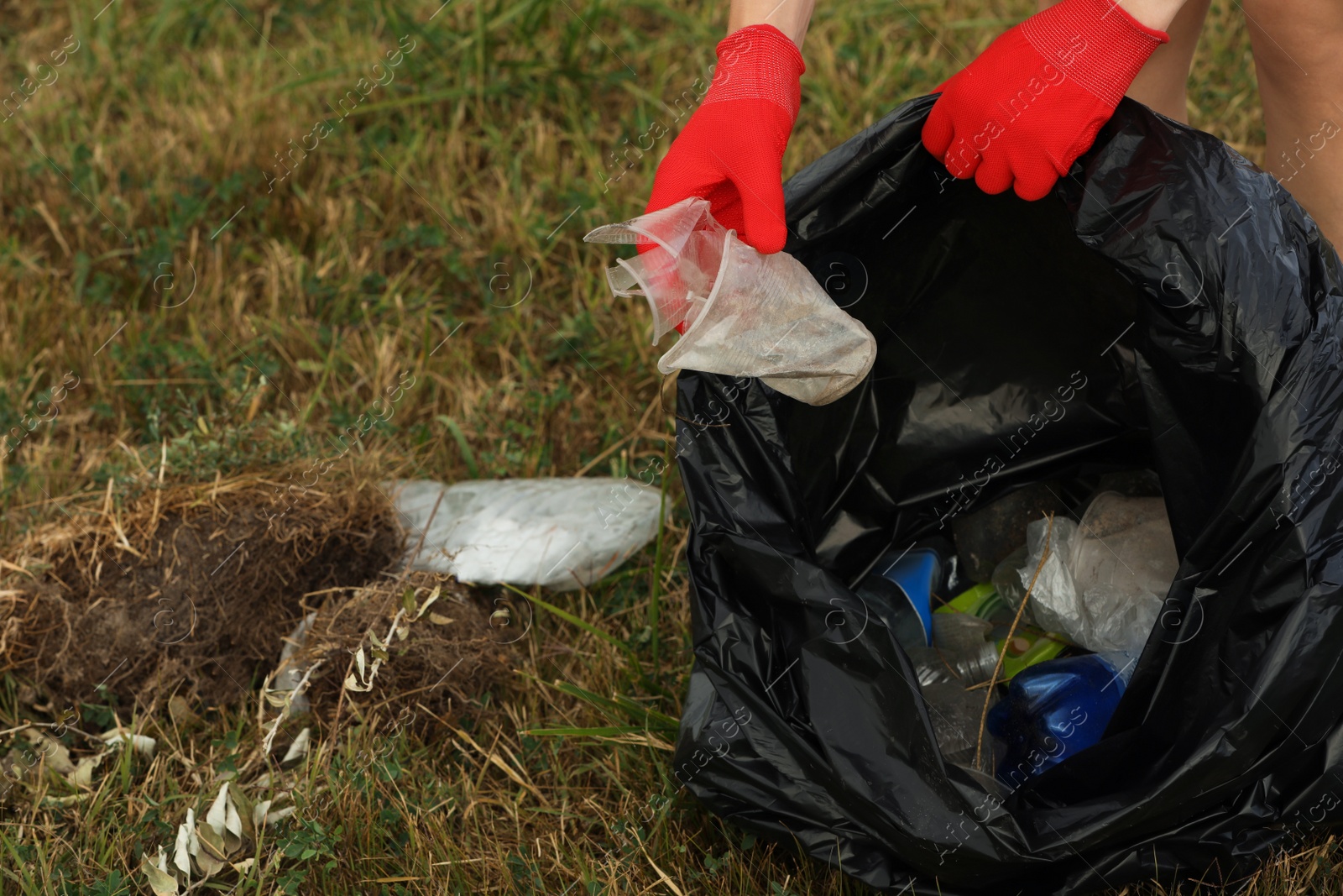 Photo of Woman in gloves with trash bag collecting garbage in nature, closeup