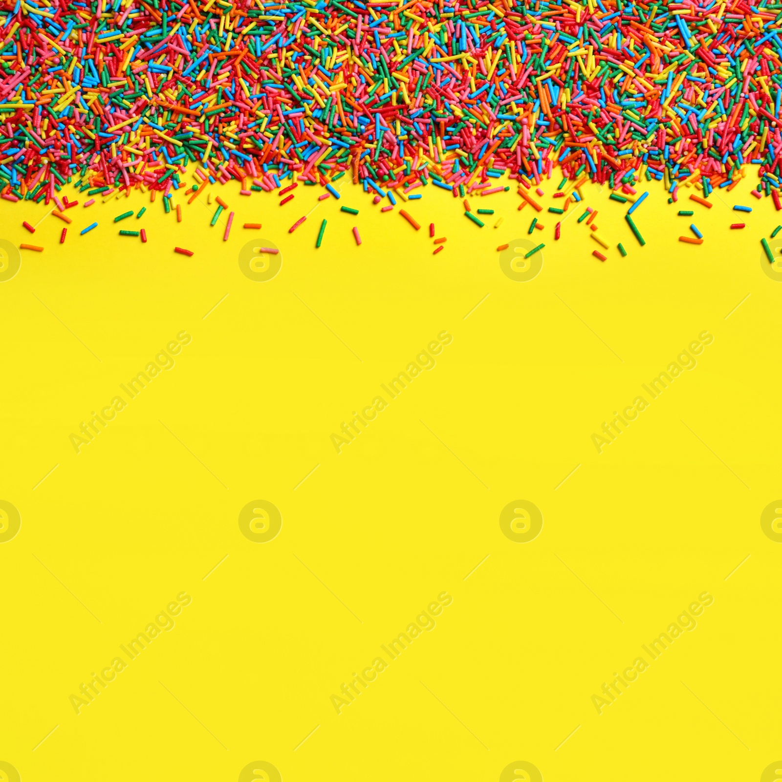 Photo of Bright colorful sprinkles on yellow background, flat lay with space for text. Confectionery decor