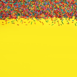 Photo of Bright colorful sprinkles on yellow background, flat lay with space for text. Confectionery decor