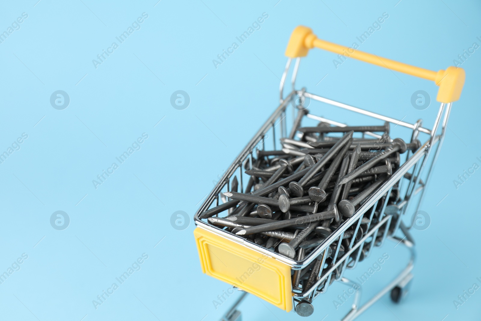 Photo of Metal nails in shopping cart on light blue background, closeup. Space for text