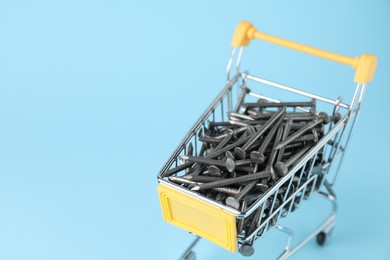 Photo of Metal nails in shopping cart on light blue background, closeup. Space for text