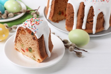 Photo of Piece of glazed Easter cake with sprinkles and painted eggs on white wooden table, space for text