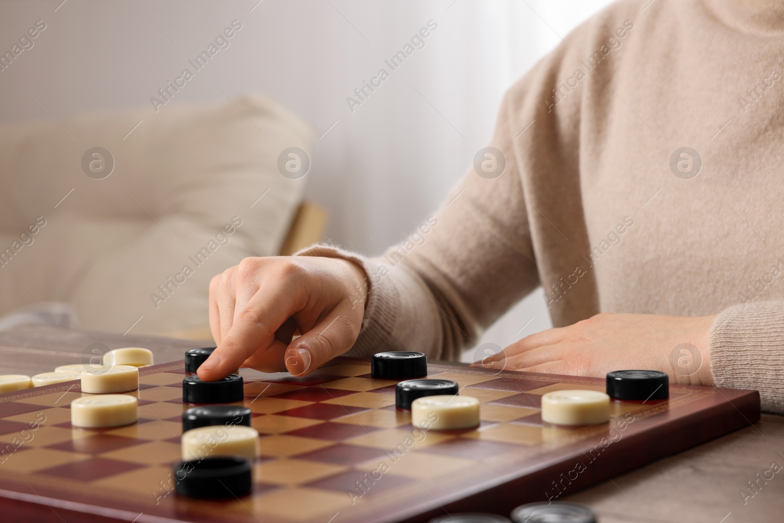 Photo of Playing checkers. Woman thinking about next move at table in room, closeup