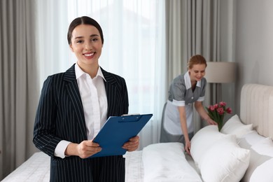 Housekeeping manager with clipboard checking maid's work in hotel bedroom