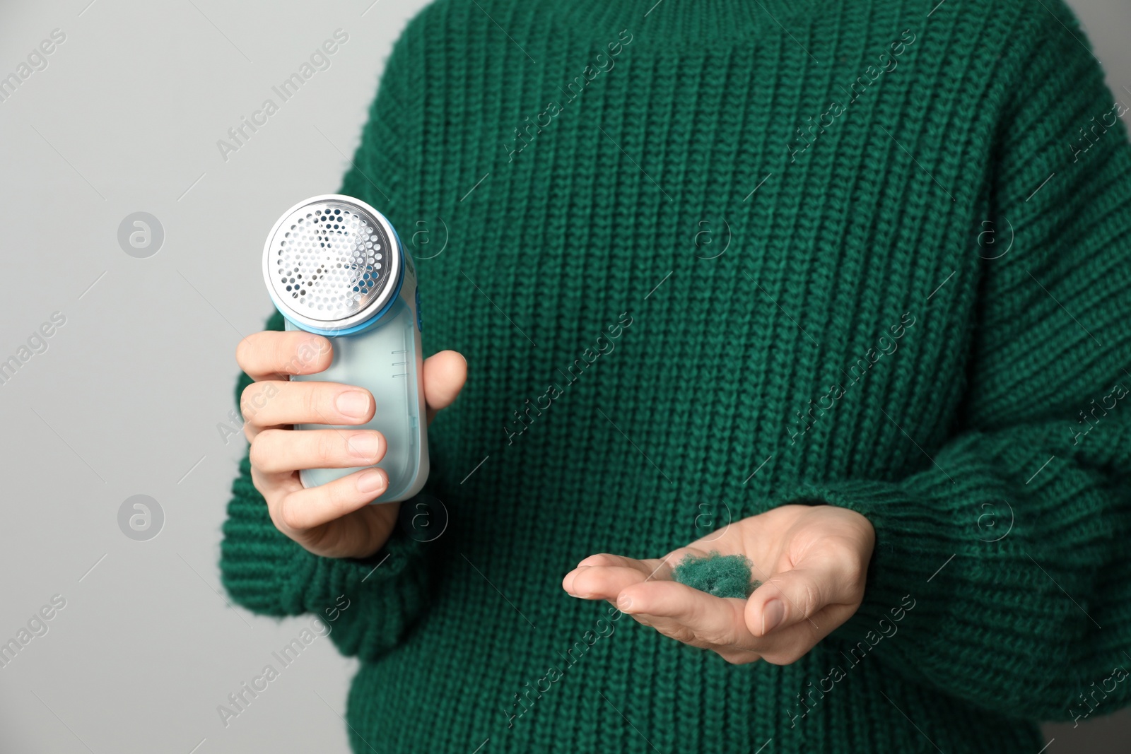 Photo of Woman in woolen sweater holding fabric shaver and lint on light grey background, closeup