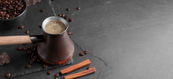 Image of Turkish coffee. Cezve with freshly brewed beverage, coffee beans, cinnamon and chocolate on dark grey table. Banner design with space for text