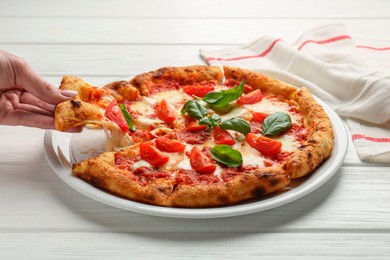 Woman taking piece of delicious Margherita pizza at white table, closeup