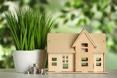 Photo of Mortgage concept. House model, coins and plant on white table against blurred background