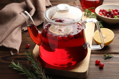 Photo of Tasty hot cranberry tea in teapot, rosemary and fresh berries on wooden table