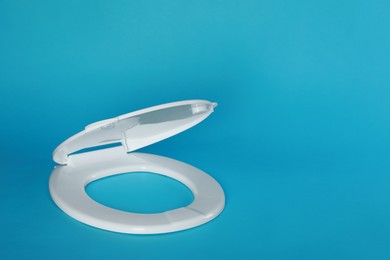 Photo of New plastic toilet seat on light blue background, space for text