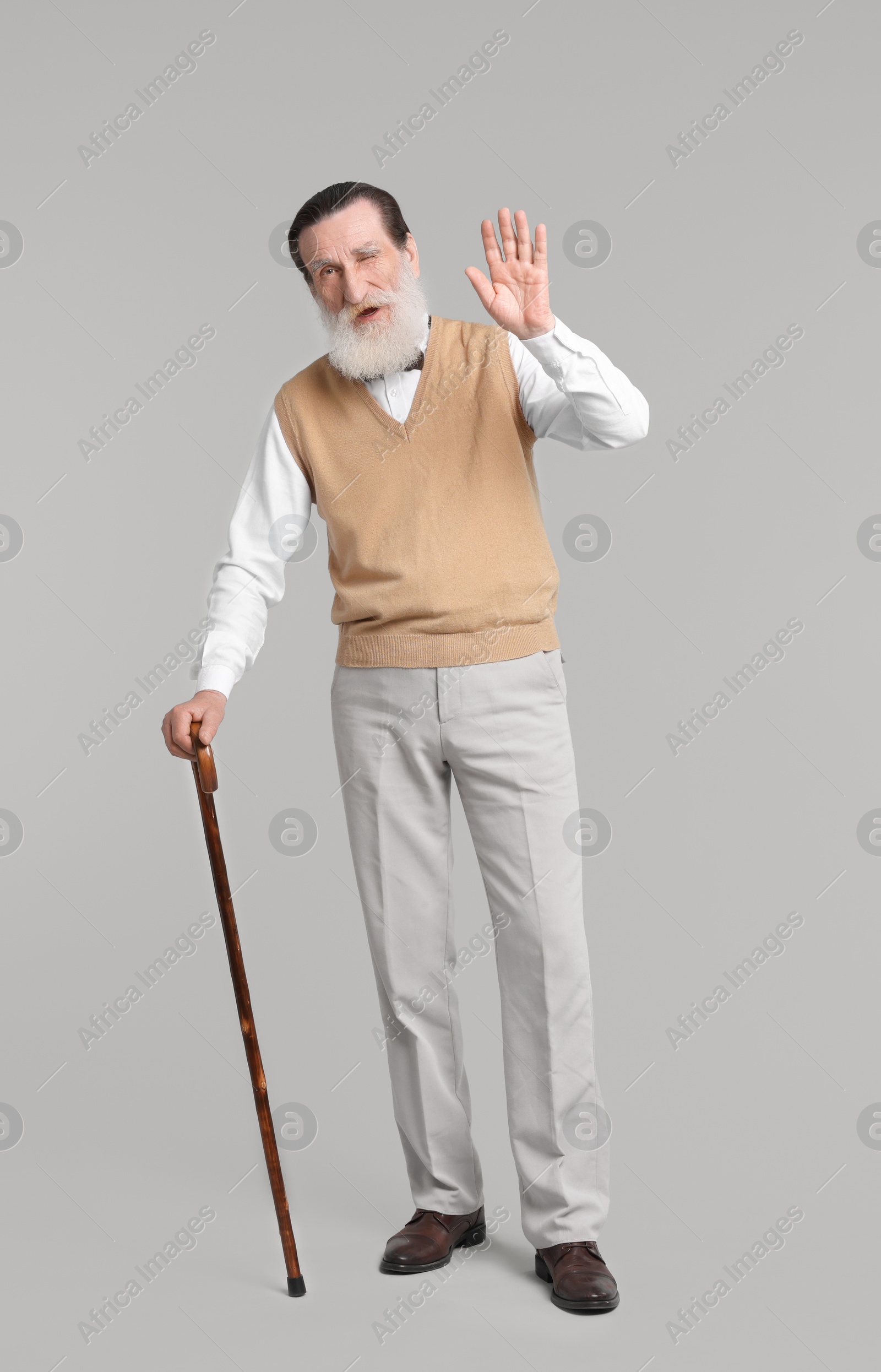 Photo of Senior man with walking cane waving on light gray background