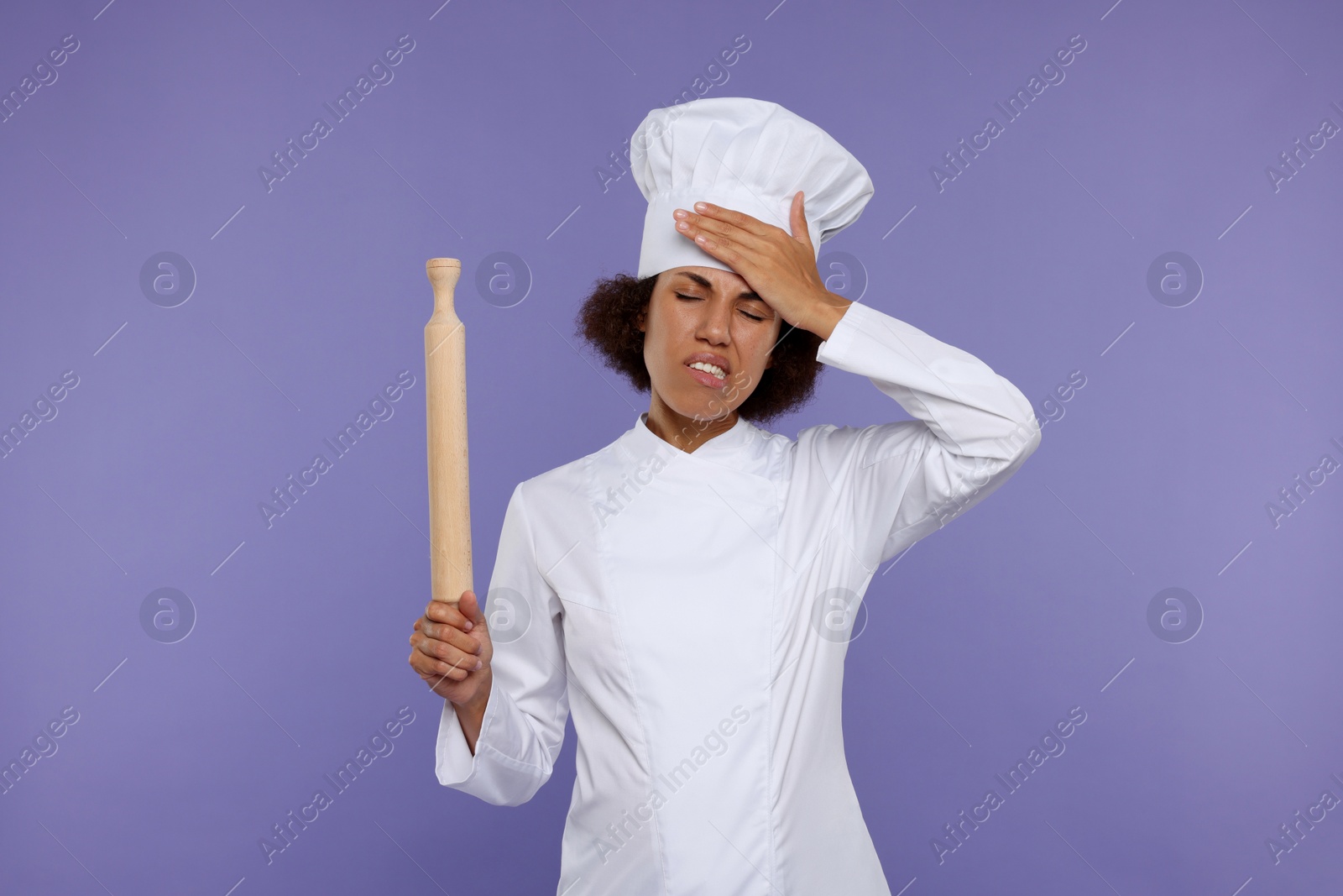 Photo of Frustrated female chef in uniform holding rolling pin on purple background