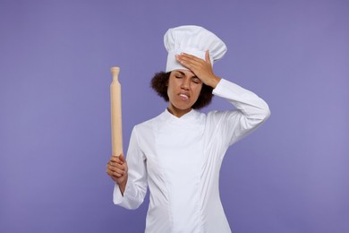 Photo of Frustrated female chef in uniform holding rolling pin on purple background