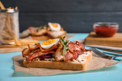 Photo of Delicious sandwich with bacon on blue table
