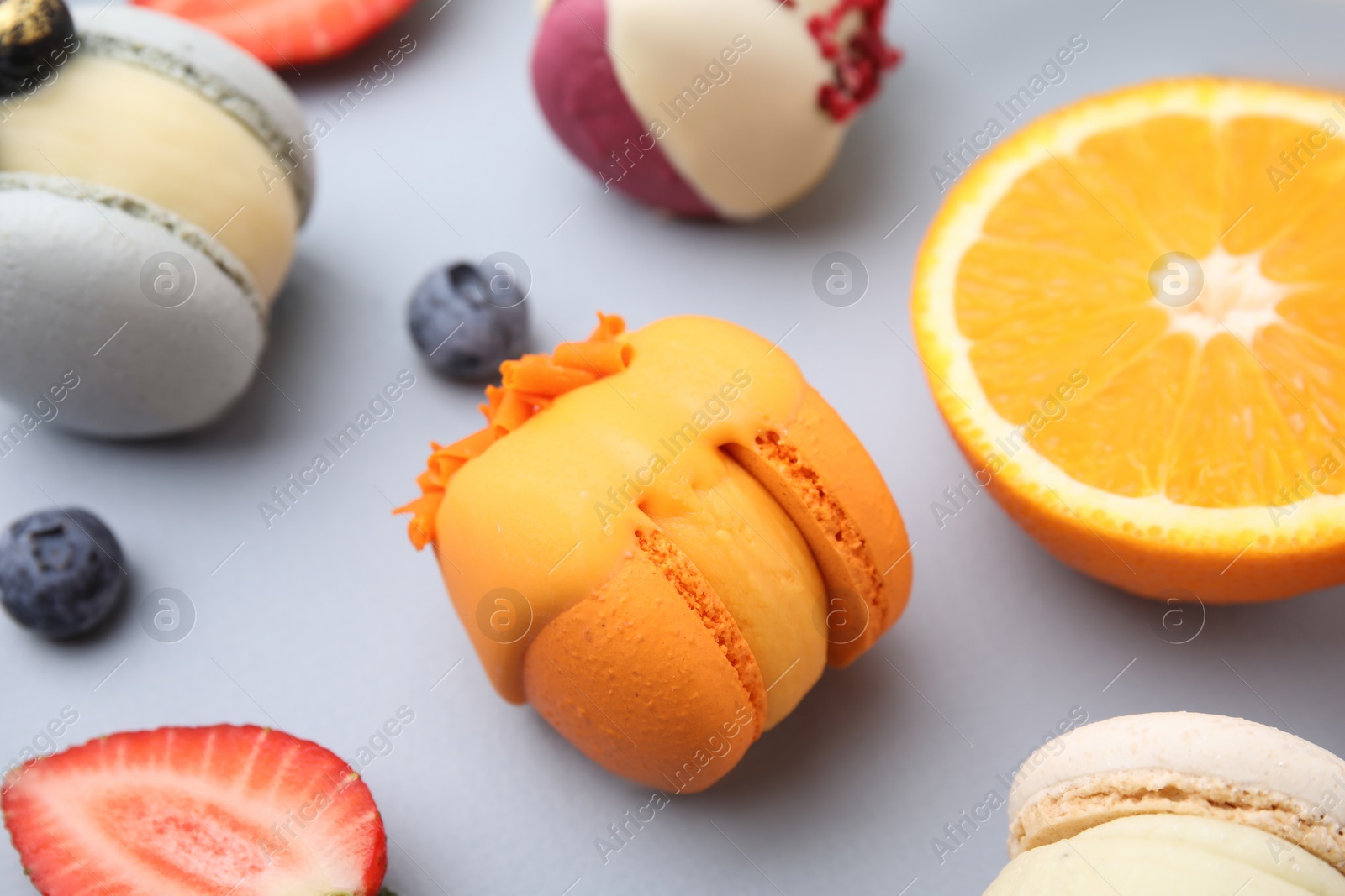 Photo of Delicious macarons, fruits and berries on light blue table, closeup