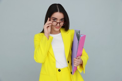 Photo of Young female intern with eyeglasses and folders on grey background