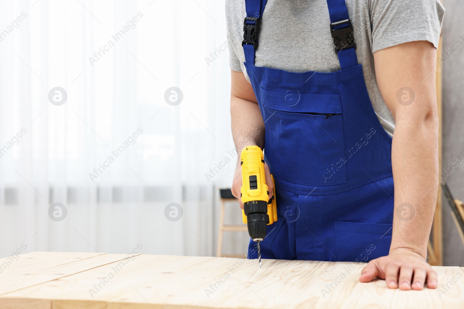 Photo of Young worker using electric drill at table in workshop, closeup