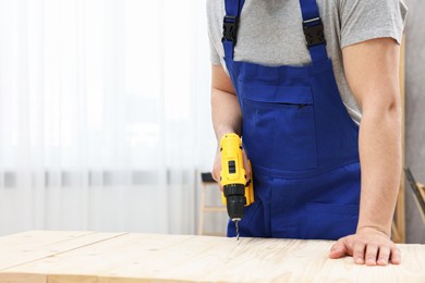 Young worker using electric drill at table in workshop, closeup