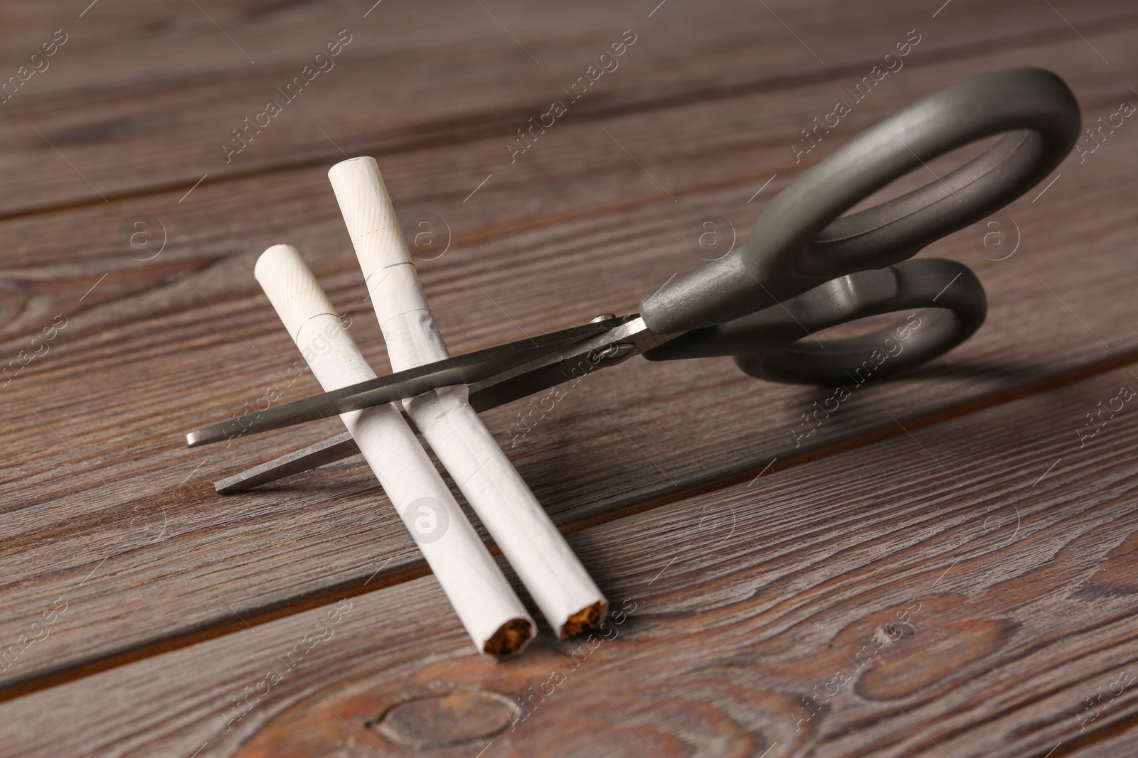 Photo of Scissors cutting cigarettes on wooden table. No smoking concept