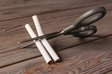 Scissors cutting cigarettes on wooden table. No smoking concept