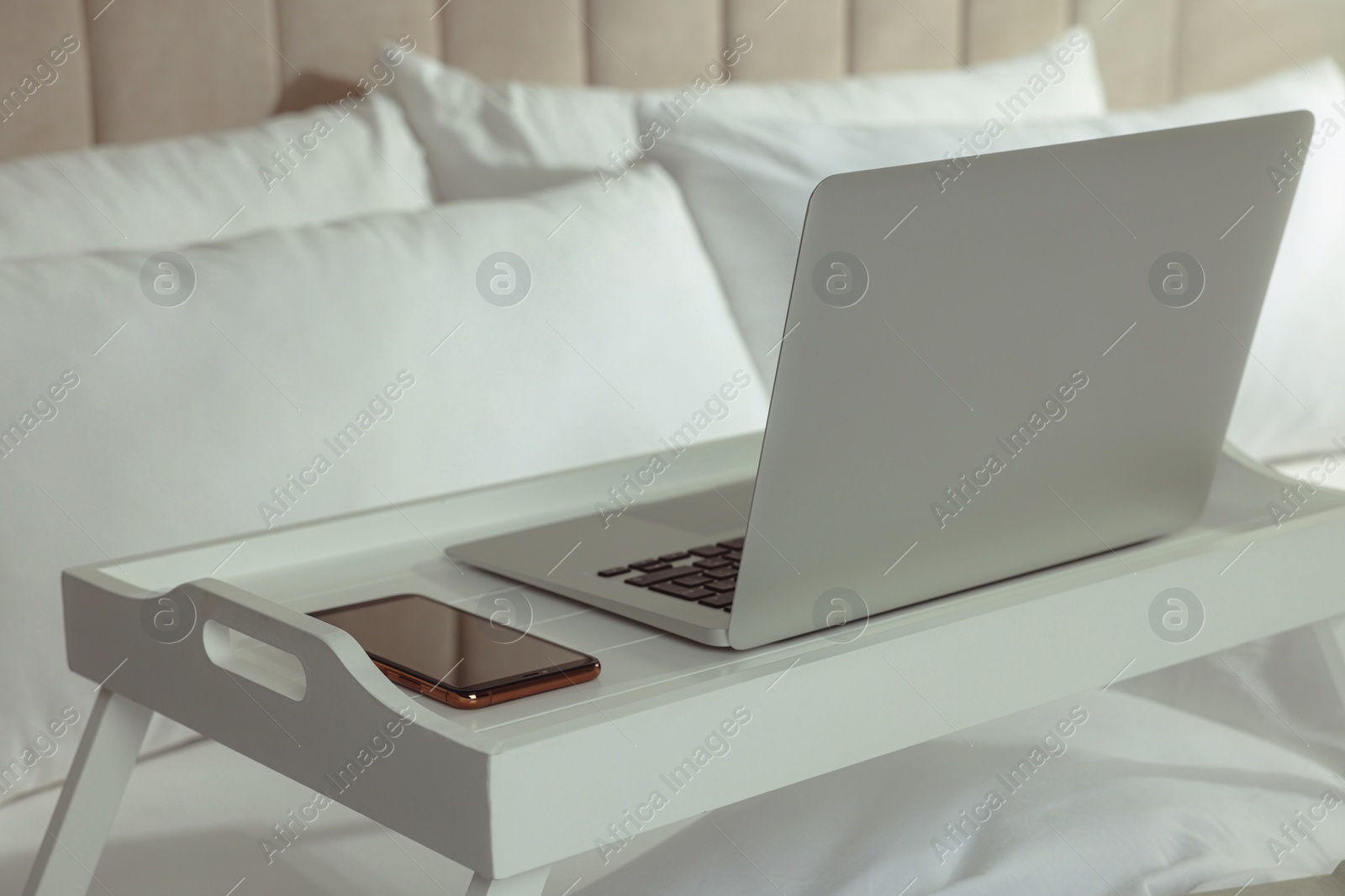 Photo of White tray with modern laptop and smartphone on bed indoors