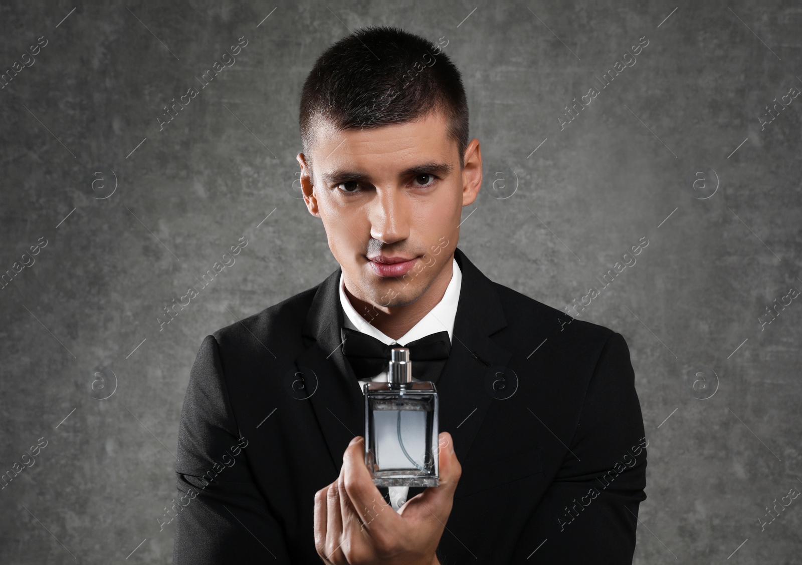 Photo of Handsome young man with bottle of perfume on grey stone background