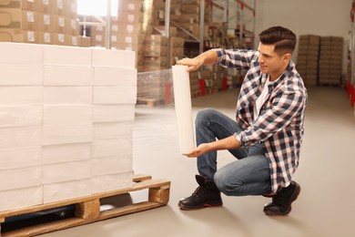 Photo of Worker wrapping boxes in stretch film at warehouse