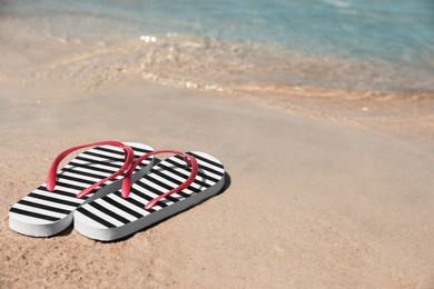 Stylish flip flops on sandy beach near sea, space for text