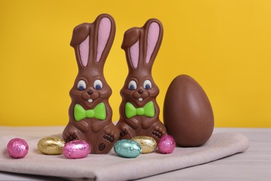 Chocolate Easter bunnies and eggs on white wooden table against yellow background