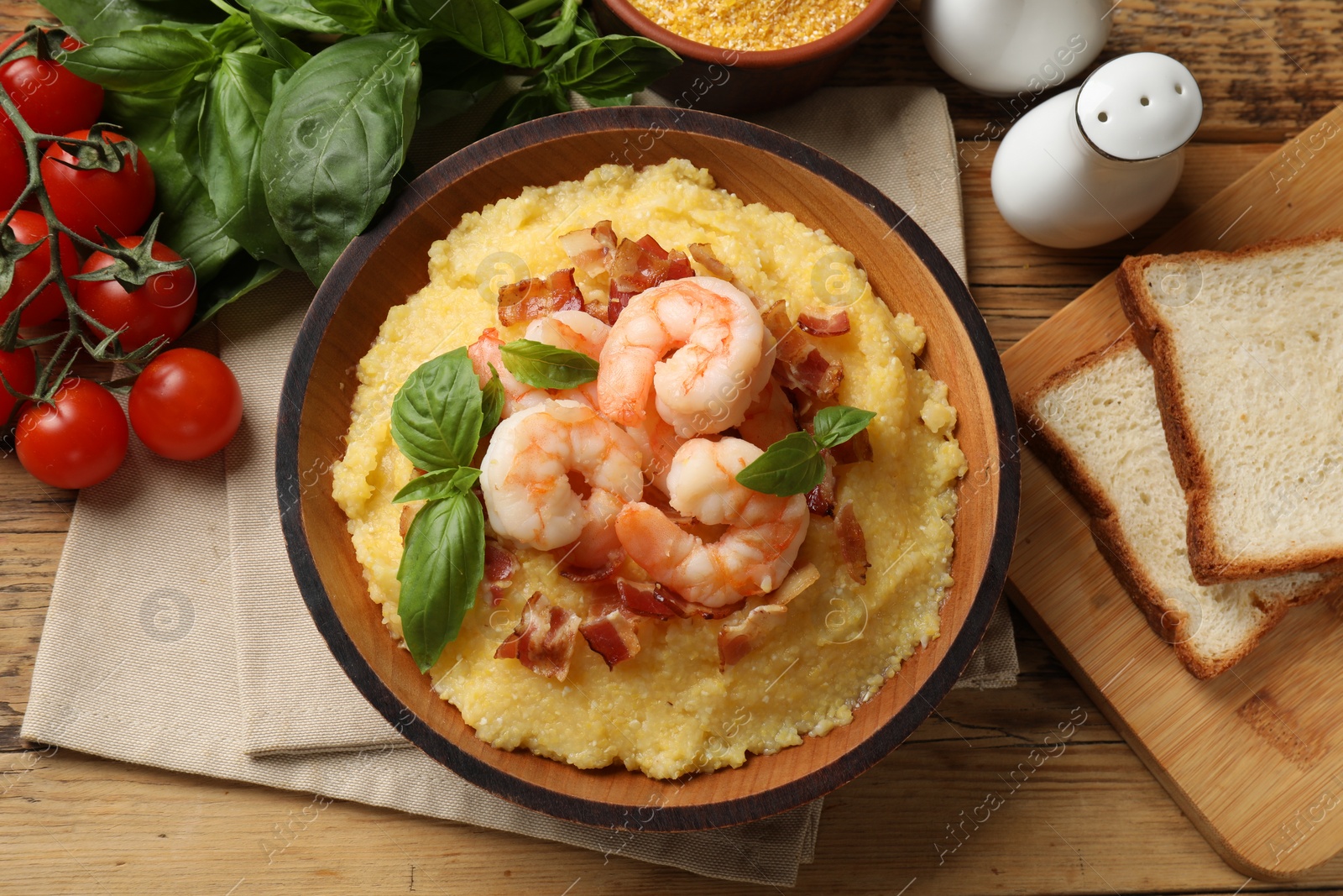 Photo of Fresh tasty shrimps, bacon, grits and basil in bowl on wooden table, flat lay