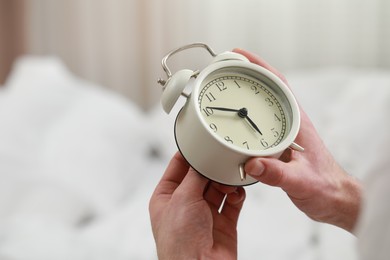 Photo of Man with alarm clock in bedroom, closeup of hands. Space for text