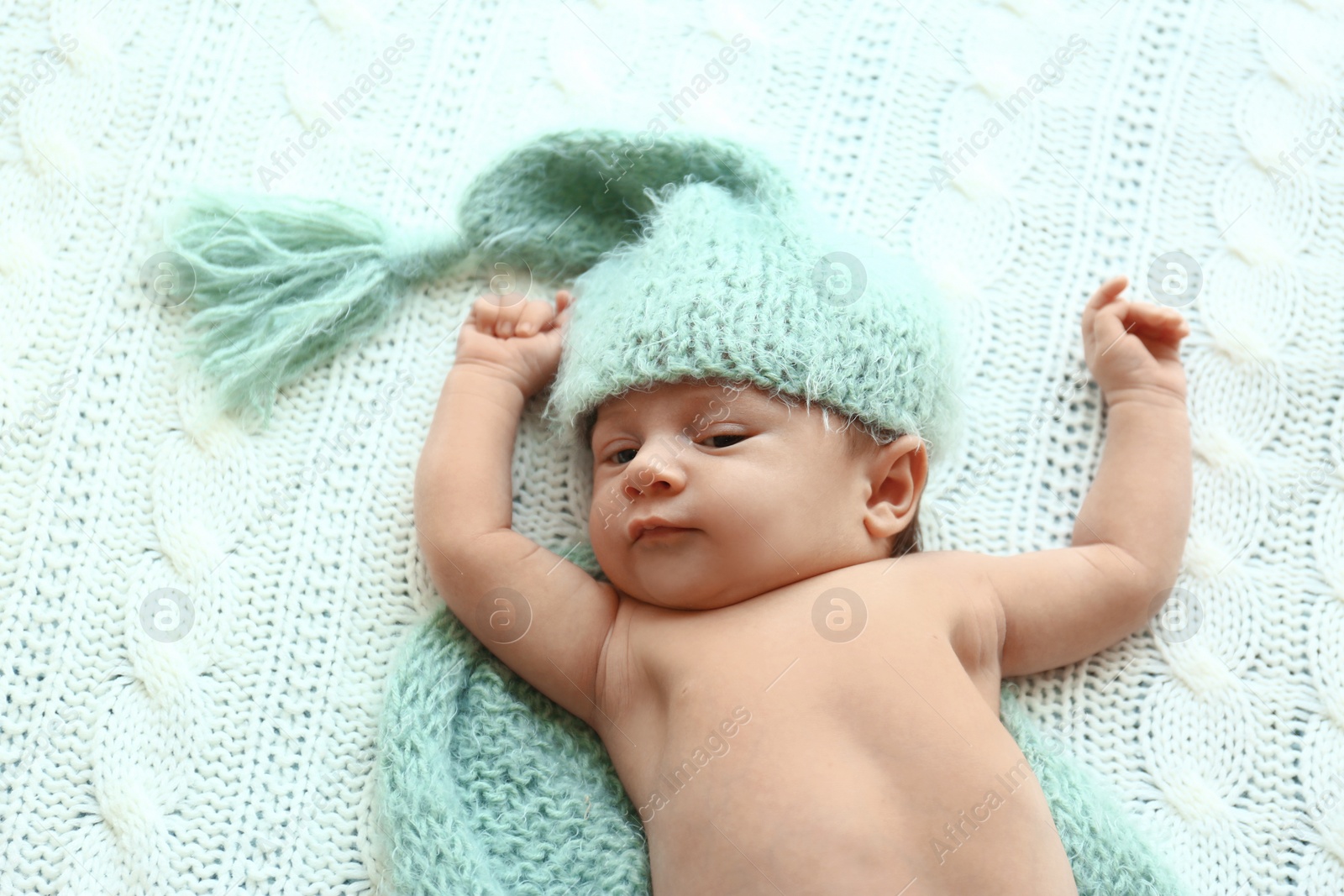 Photo of Cute little baby in green hat and plaid lying on soft blanket, top view