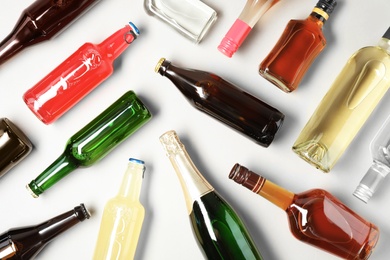 Photo of Bottles with different alcoholic drinks on light background, flat lay