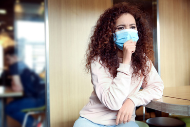 Photo of African-American woman with disposable mask in cafe. Virus protection