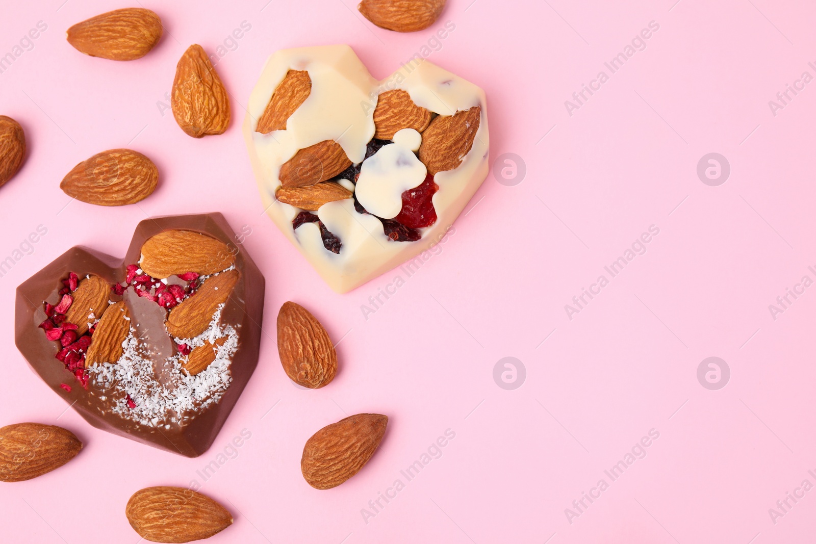 Photo of Tasty chocolate heart shaped candies with nuts on pink background, flat lay. Space for text