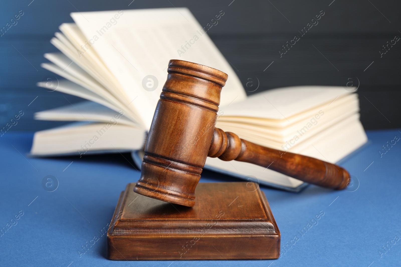 Photo of Wooden gavel, sound block and book on blue table, closeup