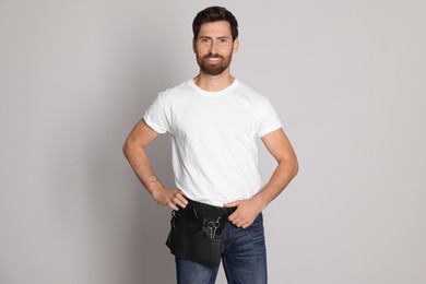 Photo of Smiling hairdresser with tool bag on light grey background