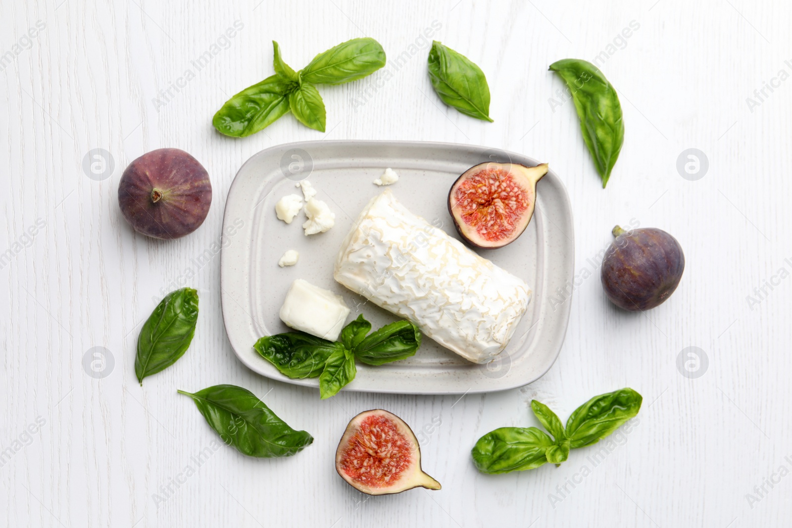 Photo of Delicious goat cheese with figs and basil on white wooden table, flat lay