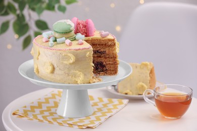 Photo of Delicious cake decorated with macarons and marshmallows and cup of tea on white table