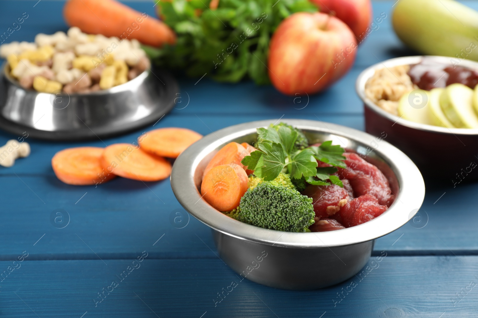 Photo of Natural pet food in feeding bowls on blue wooden table, closeup