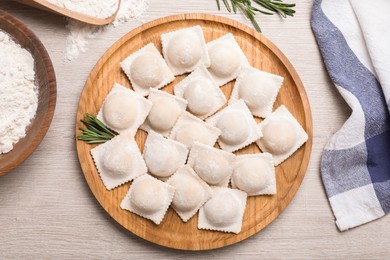 Uncooked ravioli and rosemary on white wooden table, flat lay